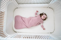 Baby i sin spjällsäng i rosa sovpåse