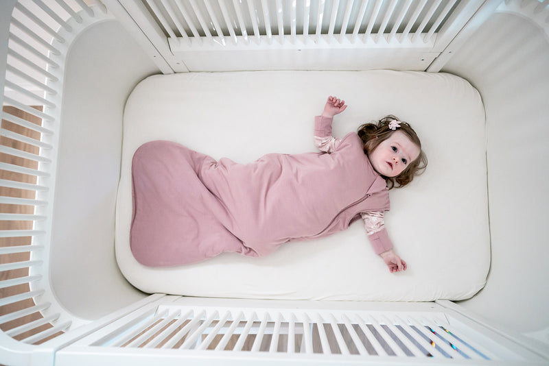 Baby i sin spjällsäng i rosa sovpåse