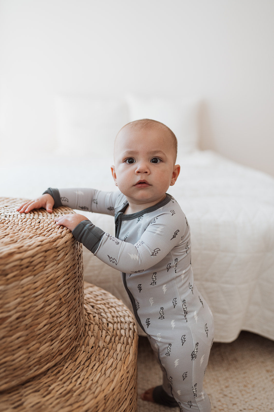 Baby står upp i grå pyjamas