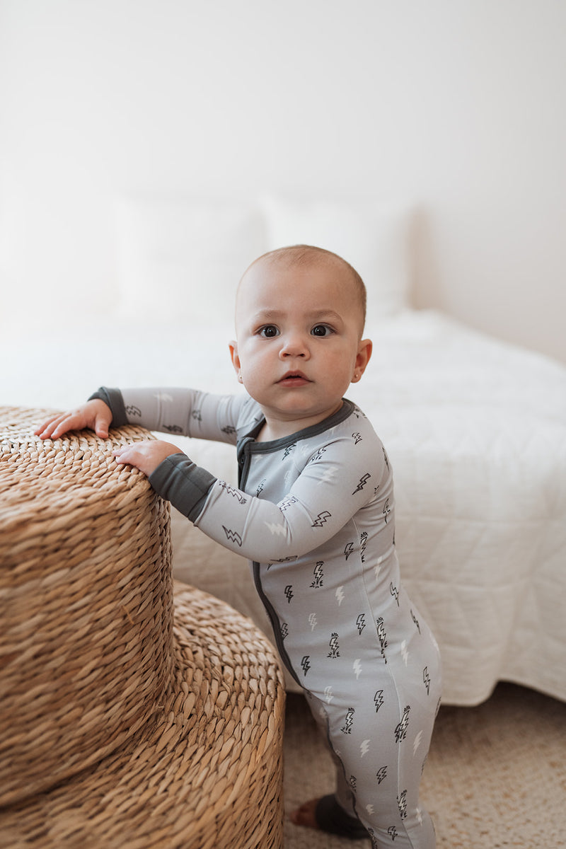 Baby står upp i grå pyjamas