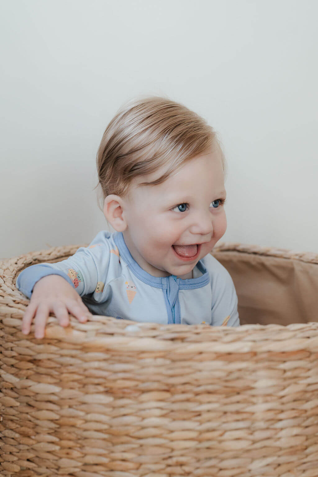 Child sitting in a wicker basket wearing a light blue outfit with colorful patterns.