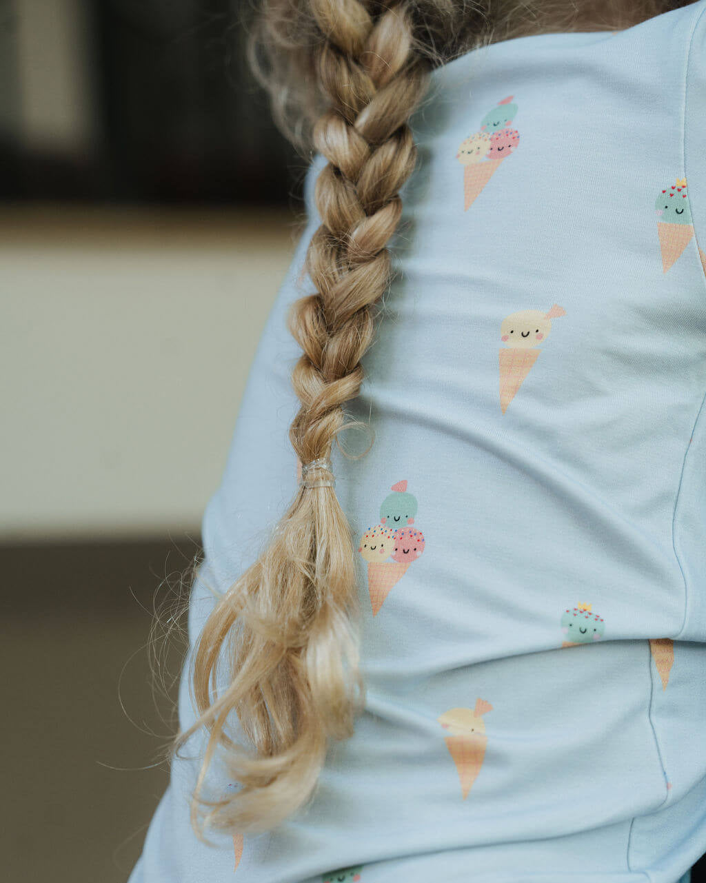 Person wearing a light blue shirt with ice cream cone pattern, focusing on braided hair.