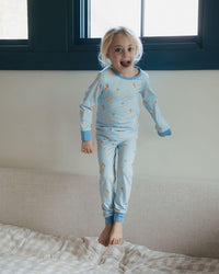 Child in light blue pajamas with star pattern jumping on a bed.