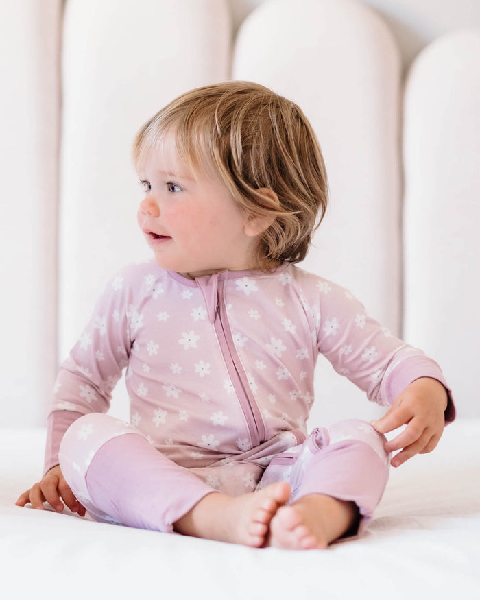 Child wearing a pink star-patterned onesie sitting on a white bed.