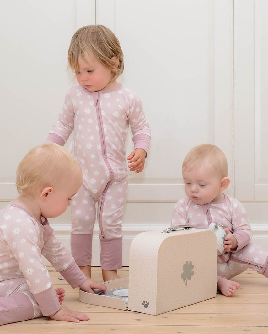 Three children playing with a wooden toy box in a room with floral wallpaper.