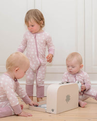 Three children playing with a wooden toy box in a room with floral wallpaper.