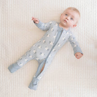 A baby lying on a textured cream blanket, wearing a light blue footed sleeper with a white sheep pattern and a front zipper.