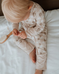 Child in a patterned onesie sitting on a bed with a wooden brush.