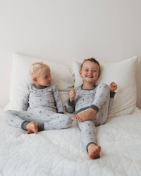 Two children in matching pajamas sitting on a bed with white pillows.