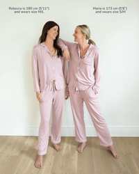 Two women wearing matching pink pajama sets with text about their heights and pajama sizes.