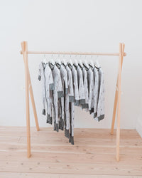 A wooden A-frame clothing rack holding multiple light gray and white patterned baby garments, set against a plain white wall and light wood floor.