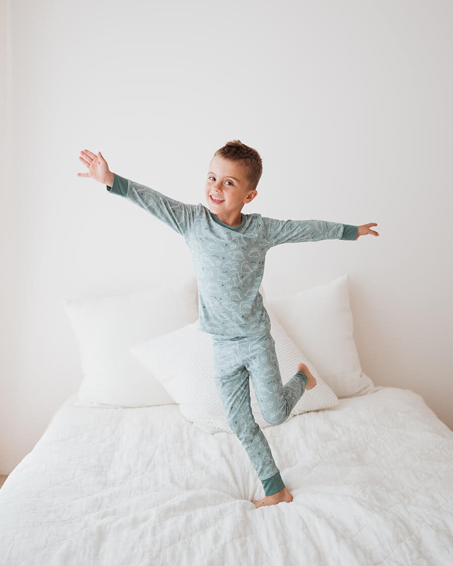 Child in gray pajamas standing on a bed with arms outstretched