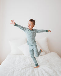 Child in gray pajamas standing on a bed with arms outstretched