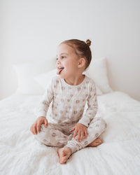 Child wearing a patterned onesie sitting on a white bed.