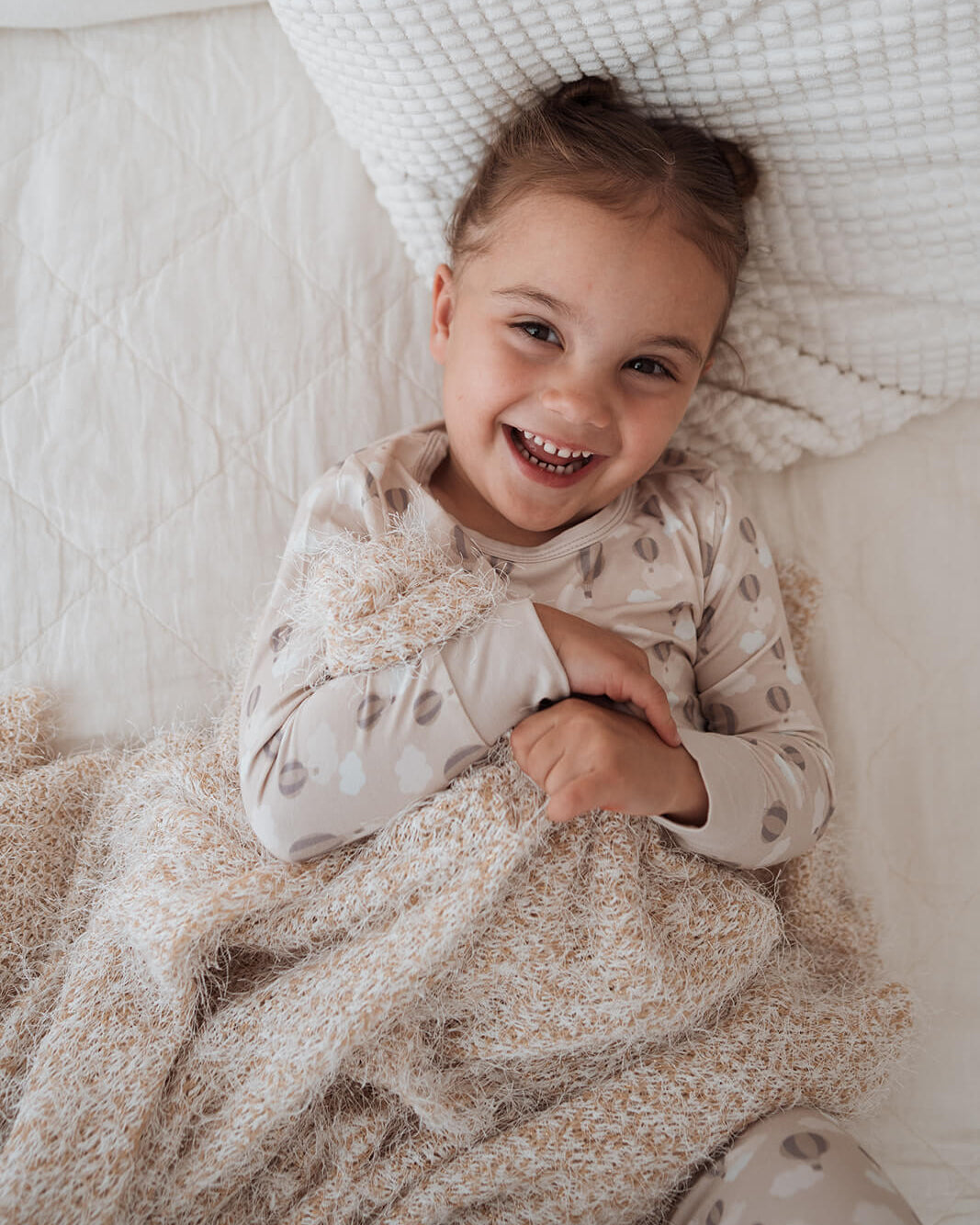Child lying on a soft surface with a smile, wearing a patterned outfit.
