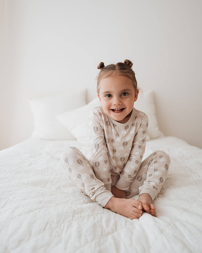 Child wearing a patterned outfit sitting on a white bed.