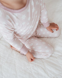 Baby in pink pajamas sitting on a white bed