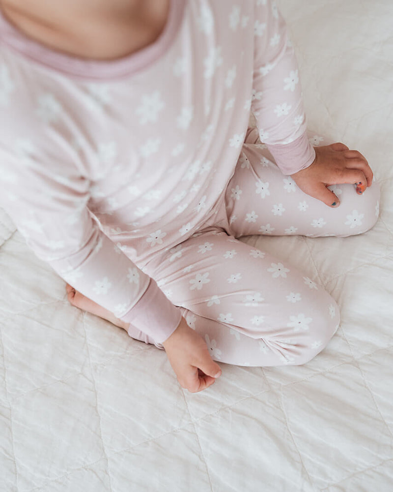 Baby in pink pajamas sitting on a white bed