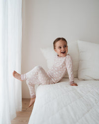 Child in pajamas sitting on a bed in a bright room