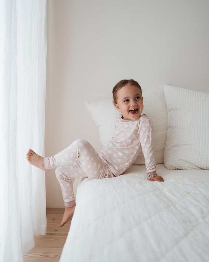 Child in pajamas sitting on a bed in a bright room