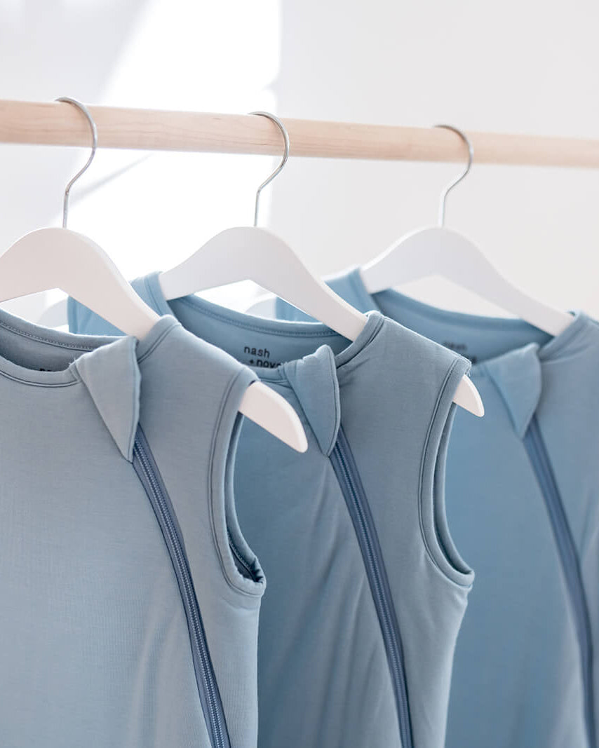Three sleeveless light blue activewear tops hanging on white hangers from a wooden clothing rack in a bright indoor setting.