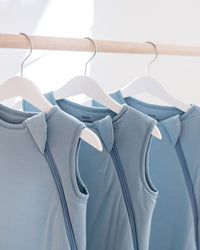 Three sleeveless light blue activewear tops hanging on white hangers from a wooden clothing rack in a bright indoor setting.