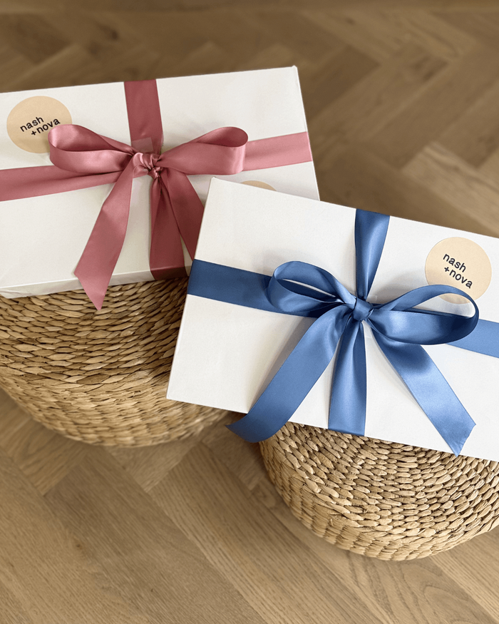 Two gift boxes with ribbons on a woven stool